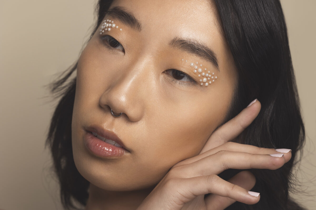 Model Maya Wang poses for a studio skincare beauty shoot. She has a natural glam look with pearls arranged artfully under her eyebrows.